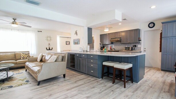 A modern kitchen with grey cabinets, a central island, and a dining area with bar stools. - Stylish 3/2 pool home near Siesta Key - Turtle House (Sarasota)