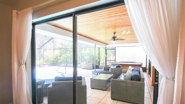 A room with a sliding glass door leading to an outdoor patio area. Inside, there are wicker sofas and a small table. - Elegant 3 BR/2 BA Private Pool Home - Florida Oasis (Palmetto)