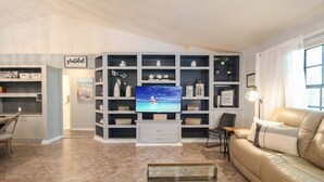 A living room with a TV, shelves, a sofa, and a coffee table. - Elegant 3 BR/2 BA Private Pool Home - Florida Oasis (Palmetto)