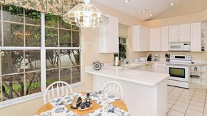 Una cocina moderna con armarios blancos, una isla central y un amplio ventanal con vistas al verdor.