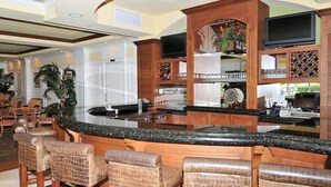 Una zona de bar con una encimera curva de granito, taburetes de madera y un televisor sobre la barra.
