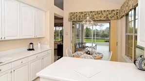 Una cocina con armarios blancos, una mesa de comedor con sillas y vistas a un jardín a través de amplios ventanales.