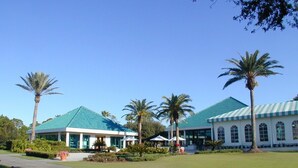 Un edificio con techo verde, palmeras y un césped bien cuidado.