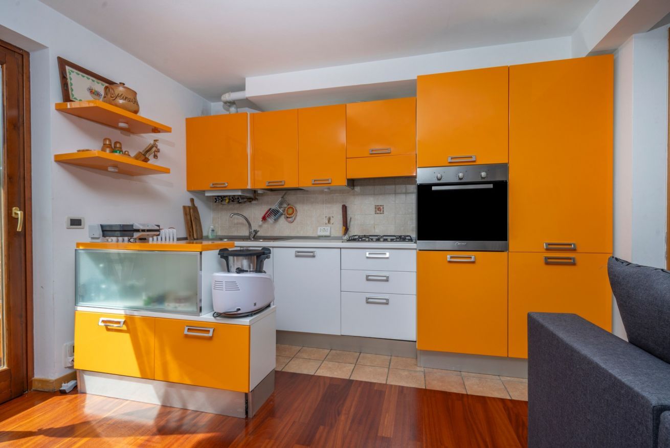 A compact kitchen with orange cabinets, a built-in oven, and a small refrigerator.