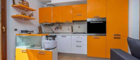 A compact kitchen with orange cabinets, a built-in oven, and a small refrigerator.