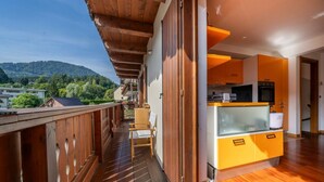 Un balcone in legno con vista su una montagna, una cucina con pensili gialli e una sedia.
