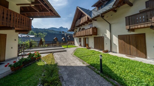 Un cortile con balconi in legno, un vialetto sterrato e vista sulle montagne.