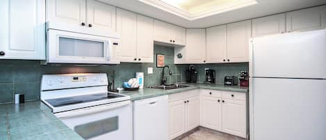 Una cocina moderna con armarios blancos, microondas, estufa, lavavajillas y refrigerador.