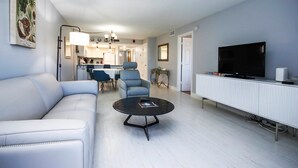 Ein modernes Wohnzimmer mit einer Couch, einem Sessel, einem Couchtisch und einem Flachbildfernseher auf einem weißen Schrank.