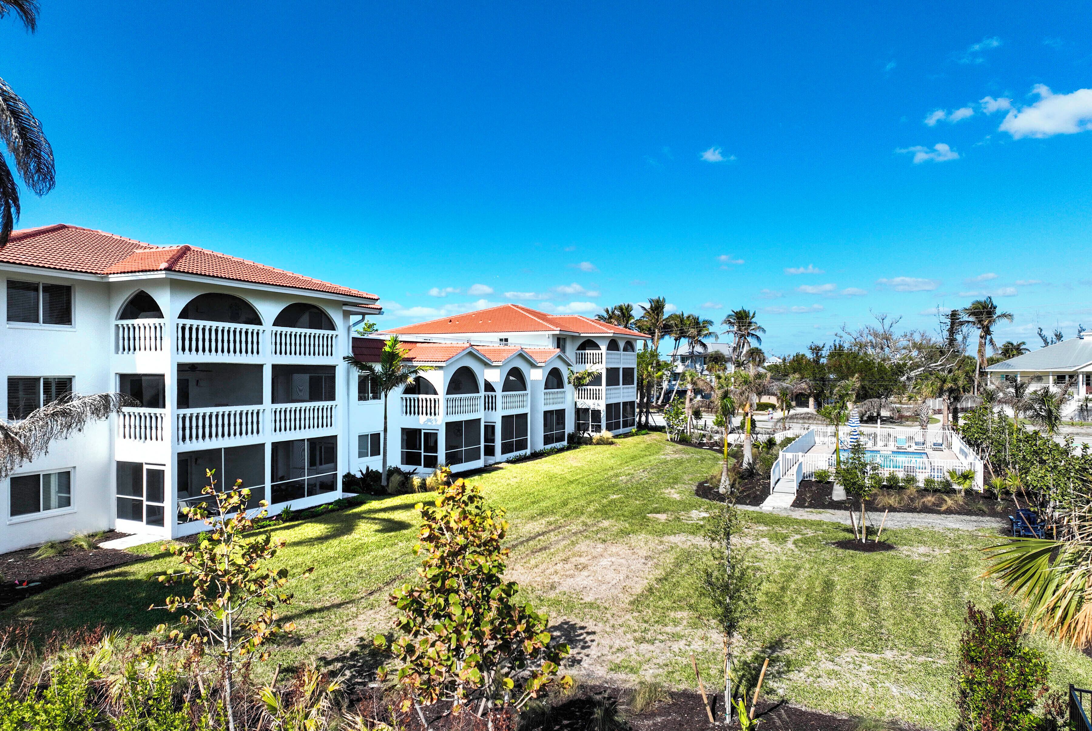 Un hotel de dos pisos con techo de tejas rojas, varios balcones y una piscina.