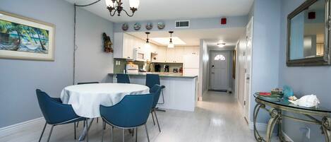 Comedor con una mesa redonda y sillas, cocina al fondo y un pasillo que conduce a otra habitación.