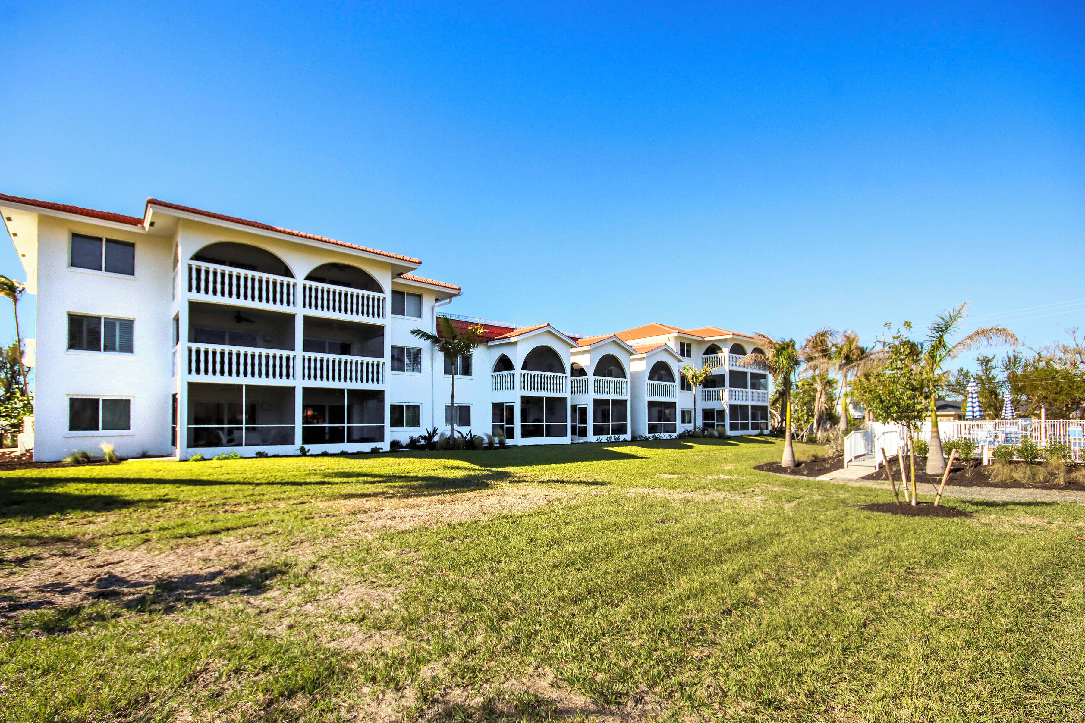 A multi-story hotel with balconies, a well-maintained lawn, and a clear blue sky.