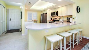 A kitchen with a central island, white bar stools, a microwave, and a refrigerator.