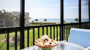 A balcony with a view of the ocean, a bowl of seashells, and a blue chair.