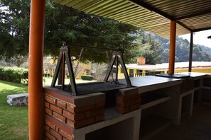 An outdoor barbecue area with a brick grill and a swing set.
