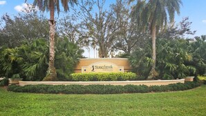A sign for Stoneybrook Golf Community with a well-maintained lawn and tropical trees.