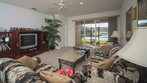 A living room with a television, sofa, coffee table, and a view of a lake through large windows.