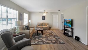 A living room with a sofa, armchair, coffee table, and a TV on a stand. - Delightful 2 BR / 2 BA Home in West Bradenton - Sans Souci (Bradenton)