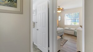 A hallway leading to a bedroom with a bed, a small table, a window, and a ceiling fan. - Delightful 2 BR / 2 BA Home in West Bradenton - Sans Souci (Bradenton)