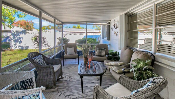 A covered patio area with wicker furniture, a central table, and large windows offering views of the outdoors. - Delightful 2 BR / 2 BA Home in West Bradenton - Sans Souci (Bradenton)