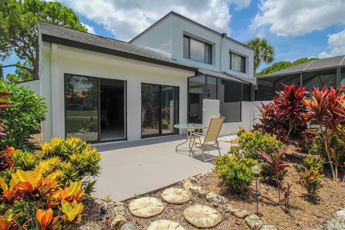 Ein modernes, zweistöckiges Haus mit großen Schiebeglastüren, einer Terrasse mit Gartenmöbeln und einem Garten mit verschiedenen Pflanzen und trittfesten Steinen.