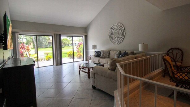A spacious living room with a sofa, coffee table, and a view through large sliding glass doors to a garden.