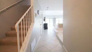A staircase with carpeted steps and white railings leading to a hallway with tiled flooring and a door at the end.