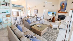 A living room with a sofa, chairs, a coffee table, and a TV. There is a bookshelf, a dining area, and a fireplace. - Spacious 3/2 pool home on Sanibel Island - 10 min walk to beach - Lily Pad (Sanibel)