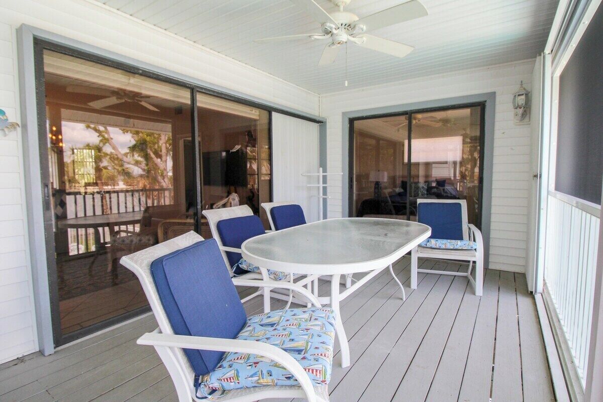 Eine überdachte Terrasse mit Glastür zu einem Deck, weißen Möbeln und einem Deckenventilator.