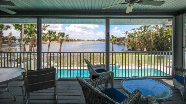 A covered outdoor area with a pool, wicker furniture, and a view of a body of water and palm trees. - Spacious 3/2 pool home on Sanibel Island - 10 min walk to beach - Lily Pad (Sanibel)