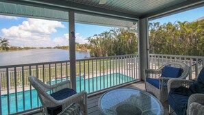 A covered outdoor area with wicker furniture, a glass table, and a view of a swimming pool and water body. - Spacious 3/2 pool home on Sanibel Island - 10 min walk to beach - Lily Pad (Sanibel)
