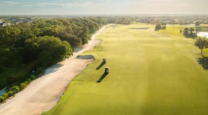 An aerial view of a golf course with sand bunkers, a water hazard, and a clear sky.