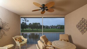 Un balcón con mobiliario de mimbre, ventilador de techo y vistas a un campo de golf.