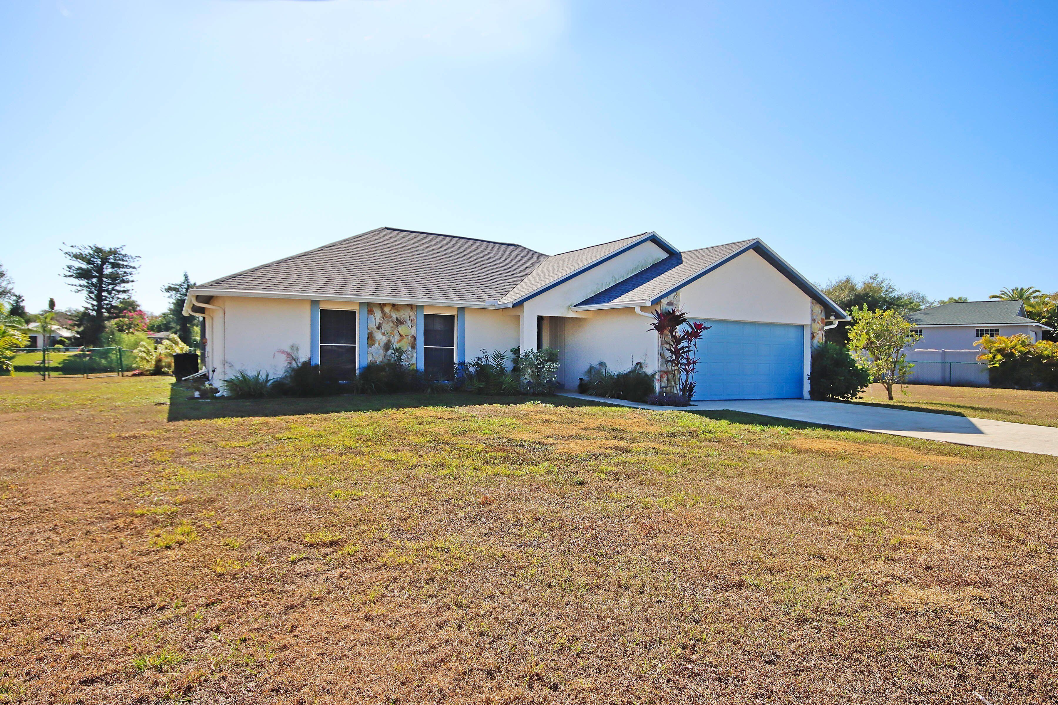 A single-story house with a sloped roof, a garage, and a front yard with sparse grass.