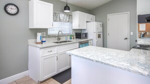 Une cuisine avec des meubles blancs, un four à micro-ondes, un réfrigérateur et une horloge au mur.