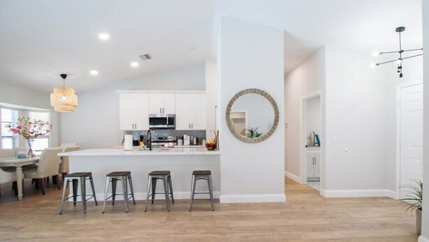 Una cocina moderna con armarios blancos, una isla central con taburetes y un espejo redondo en la pared.