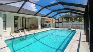 Una piscina con zona techada, agua azul cristalina y un patio con mobiliario exterior.