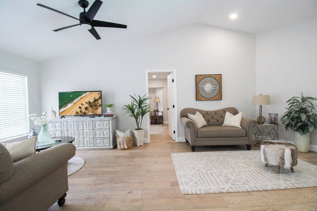 A spacious living room with a ceiling fan, a beige sofa, a coffee table, and a TV on a white cabinet.