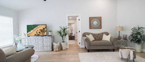 A spacious living room with a ceiling fan, a beige sofa, a coffee table, and a TV on a white cabinet.