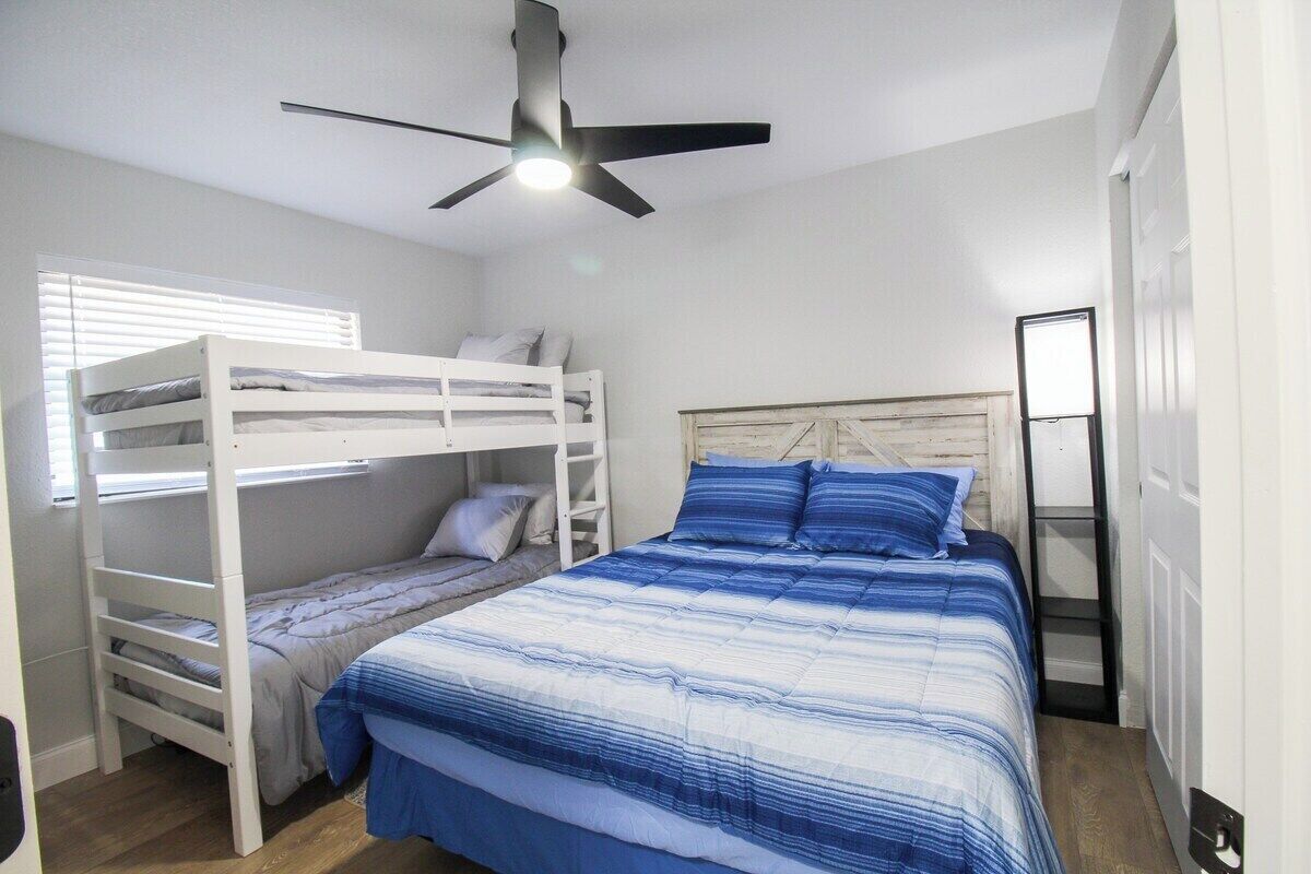 Un dormitorio con literas, ventilador de techo y ventana con persianas.