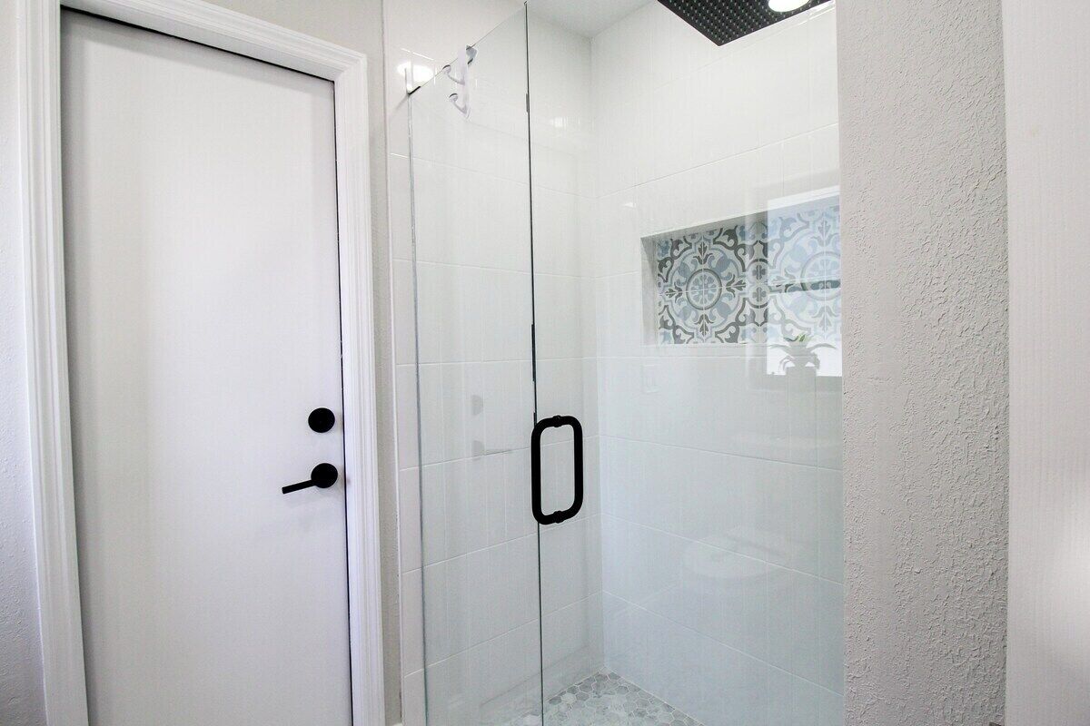 A white door with a black handle, a glass shower enclosure, and a patterned tile backsplash.