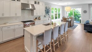 A modern kitchen with white cabinetry, a large island with bar stools, a stainless steel range hood, and a view to a balcony with outdoor furniture. - Exquisite 3 BR / 3.5 BA home with pool and spa on Longboat Key - The Captain's Quarters (Longboat Key)