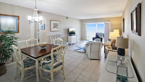 A spacious living area with a dining table, chairs, a sofa, and a TV. There is a large window providing a view of the outdoors. - Magnificent Oceanfront 2 BR Condo in Longboat Key - The Lookout (Florida)