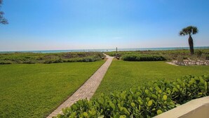 A paved pathway leading to a beach area with a palm tree and outdoor seating. - Magnificent Oceanfront 2 BR Condo in Longboat Key - The Lookout (Florida)