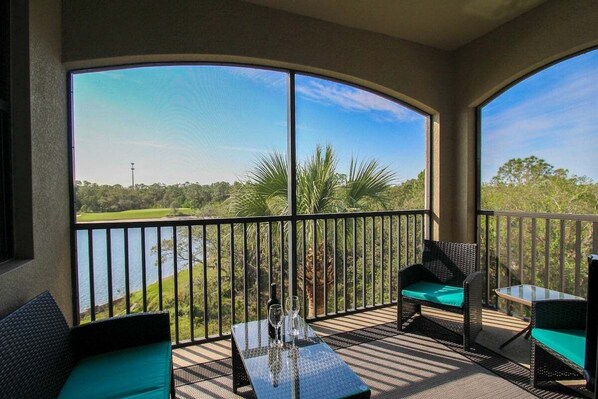 Ein Balkon mit Blick auf einen See, Korbmöbel und ein Glastisch.