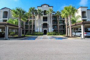 A multi-story hotel with a central entrance, palm trees, and a parking lot with handicapped spaces. - Exquisite 2 BR / 2 BA Lake Front Condo In Lakewood National Golf Club - Precious Gem (Lakewood Ranch)