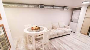Un espacio habitable compacto con una mesa redonda de comedor, un sofá blanco y una pequeña kitchenette.