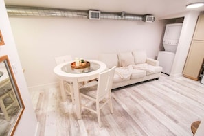 Een knus woongedeelte met een ronde eettafel, een witte bank en een kleine keukenhoek.
