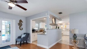Un salón amplio con suelo de madera, ventilador de techo, decoración de caballito de mar y vistas al área de cocina y comedor.