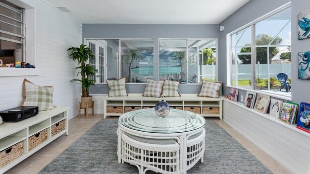 Una habitación acogedora con un banco blanco, una mesa de vidrio y vistas al océano a través de amplios ventanales.